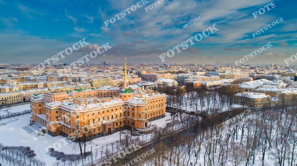На фотографии изображён Михайловский замок в зимнем убранстве. Яркий фасад замка контрастирует с белоснежным пейзажем вокруг. На заднем плане открывается вид на историческую часть Санкт-Петербурга. Это уникальный памятник архитектуры с богатой историей, расположенный в центре города.